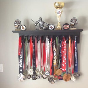 May include: A black wooden shelf with a hockey player figurine, a trophy, and several hockey pucks. Hanging from the shelf are a variety of colourful medals with ribbons.