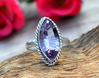 May include: A silver ring with a large, faceted, marquise-shaped amethyst gemstone. The ring has a twisted band and a decorative border around the stone.