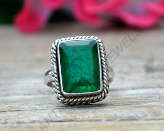 Puede incluir: Un anillo de plata con una gran piedra preciosa verde esmeralda engastada en un borde de cuerda.