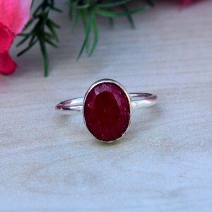 May include: A silver ring with a red oval gemstone. The ring is simple and elegant.