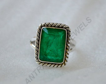 Puede incluir: Un anillo de plata con una esmeralda verde engastada en un bisel cuadrado con un borde de cuerda.