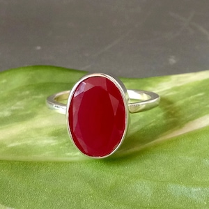 May include: A silver ring with a large, oval-shaped, red gemstone.