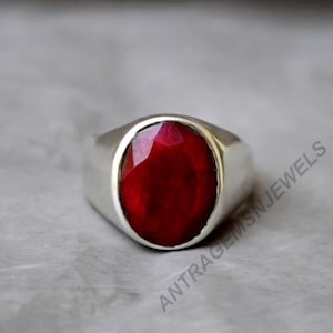 May include: A silver ring with a large, oval-shaped, red gemstone. The ring has a simple, classic design.