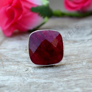 May include: A square-shaped ruby ring set in sterling silver. The ruby is a deep red color and has a faceted cut. The ring is a simple design and would make a beautiful gift.