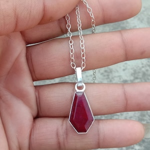 May include: A silver chain necklace with a pendant featuring a faceted, deep red gemstone.