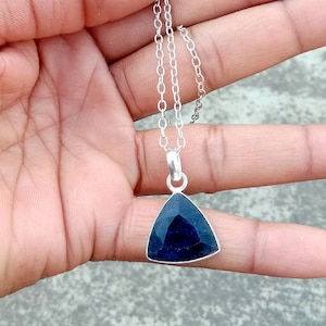 Op de afbeelding: Een zilveren ketting met een driehoekige hanger met een donkerblauwe edelsteen.