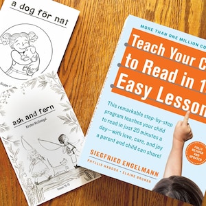 May include: Three books on a wooden surface. One book has the title "Teach Your Child to Read in 100 Easy Lessons". Two smaller books are titled "a dog for nat" and "ash and fern". The image includes illustrations and text.