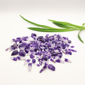 Könnte beinhalten: Ein großer Haufen Amethyst-Splitter in verschiedenen Violett- und Weißtönen. Die Splitter sind auf einer weißen Oberfläche verstreut.
