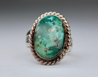 May include: A silver ring with a green turquoise stone set in a rope-like design.