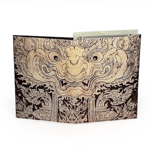 May include: A brown and beige wallet with a detailed illustration of a mythical creature's face. The wallet is open, revealing a glimpse of a folded bill inside. The design features intricate patterns and a vintage aesthetic.