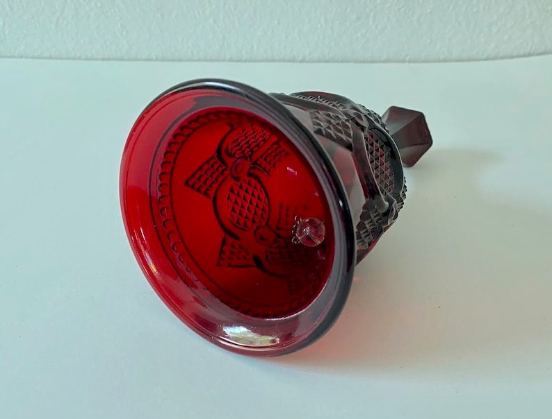 Puede incluir: Una campana de vidrio roja con un dise&ntilde;o detallado. La campana tiene una superficie texturizada y una peque&ntilde;a perilla en la parte superior.
