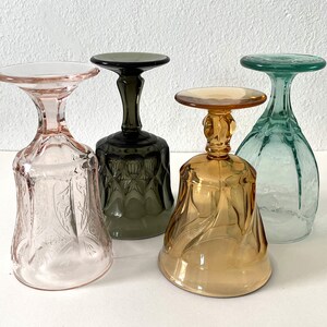 May include: Four vintage glass goblets in different colours: pink, green, brown, and amber. Each goblet has a unique etched design.