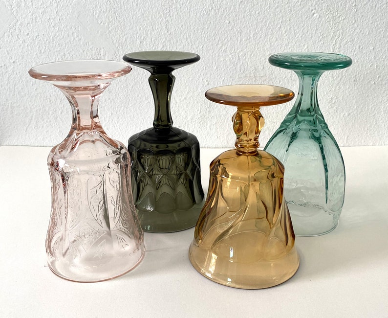 May include: Four vintage glass goblets in different colours: pink, green, brown, and amber. Each goblet has a unique etched design.