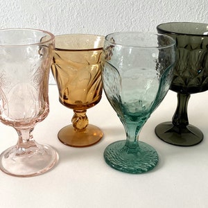 May include: Four vintage stemmed glasses in different colours and patterns. The glasses are pink, amber, green, and grey.