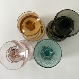 May include: Four vintage glass drinking glasses with different colours and textures. The glasses are clear, pink, green, and brown.