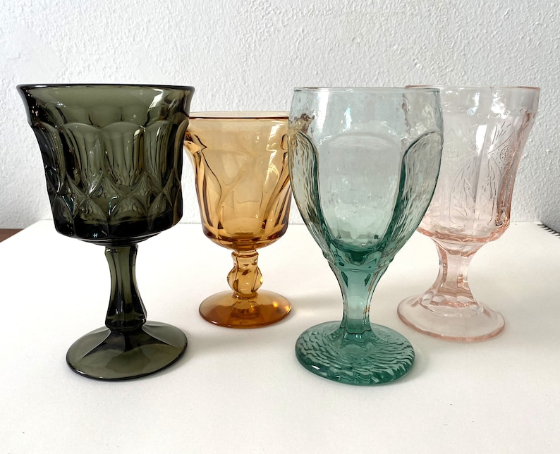 May include: Four stemmed glasses in different colours and patterns. The glasses are clear, amber, green, and pink.