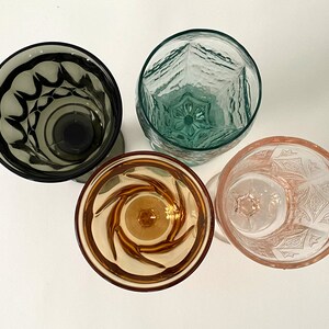 May include: Four vintage drinking glasses with different patterns. The glasses are clear, green, brown, and pink.
