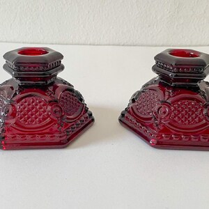Puede incluir: Dos candelabros de vidrio rojo con un dise&ntilde;o geom&eacute;trico. Los candelabros son octogonales y tienen un borde elevado alrededor de la parte superior.