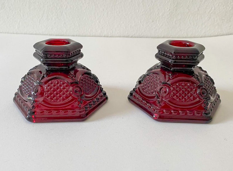 Puede incluir: Dos candelabros de vidrio rojo con un dise&ntilde;o geom&eacute;trico. Los candelabros son octogonales y tienen un borde elevado alrededor de la parte superior.