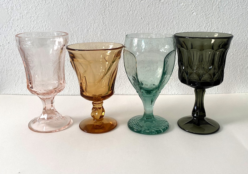 May include: Four stemmed glasses in different colours: pink, amber, green, and grey. The glasses are all similar in shape and have a textured design.