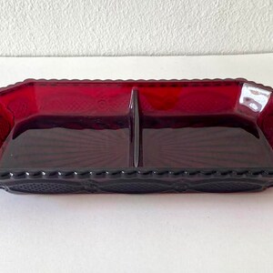 Puede incluir: Un plato de servir dividido en dos secciones, hecho de vidrio rojo con un patr&oacute;n decorativo. El plato tiene una forma rectangular.
