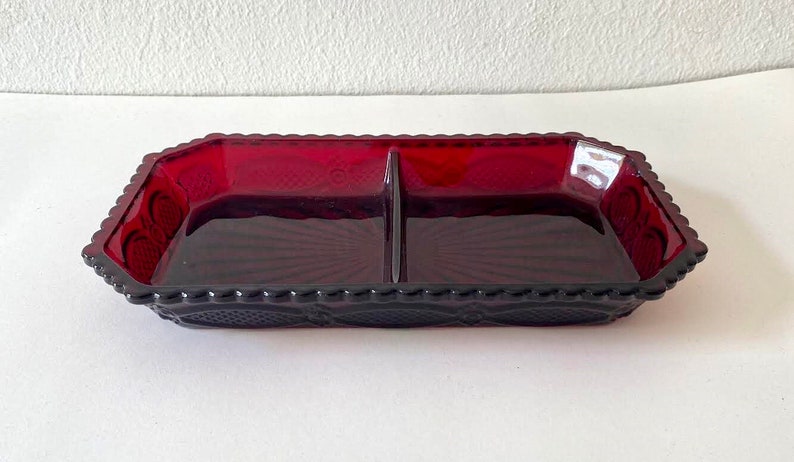 Puede incluir: Un plato de servir dividido en dos secciones, hecho de vidrio rojo con un patr&oacute;n decorativo. El plato tiene una forma rectangular.