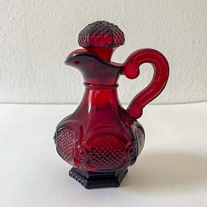 Puede incluir: Una botella de vidrio roja con un tap&oacute;n decorativo y un asa. La botella tiene un patr&oacute;n de diamante y un dise&ntilde;o en relieve.
