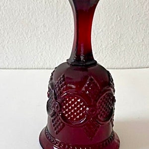 Puede incluir: Una campana de vidrio roja con un patr&oacute;n decorativo. La campana tiene una base ancha y un cuello estrecho.