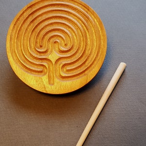 May include: A wooden circular labyrinth with a carved design and a wooden stick for tracing the path.