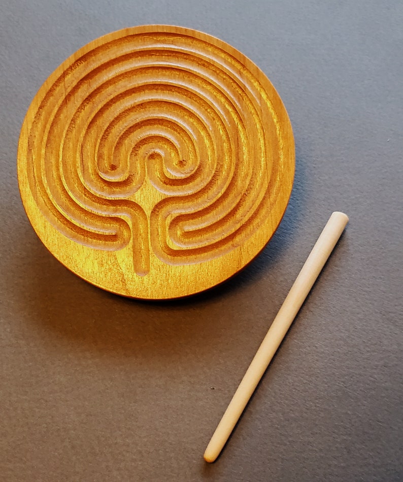 May include: A wooden circular labyrinth with a carved design and a wooden stick for tracing the path.