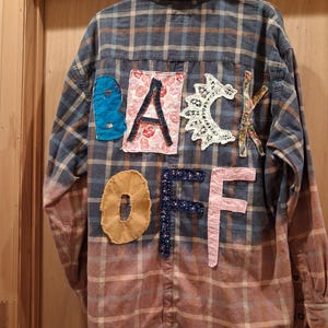 May include: Plaid button-down shirt with a faded pink and blue ombre effect. The back of the shirt features the words "BACK OFF" in various fabric patches, including blue, floral, and lace.