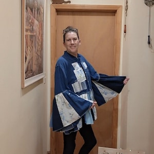 May include: A long-sleeved blue denim shirt featuring a patchwork design with floral and plaid fabric inserts, a mandarin collar, and wide flared sleeves. The shirt is paired with black leggings and light-colored canvas sneakers.