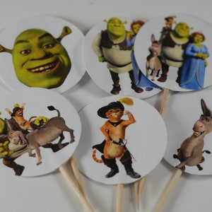 May include: Set of 6 round cupcake toppers featuring characters from the Shrek movie franchise. The toppers feature Shrek, Fiona, Donkey, Puss in Boots, and a close-up of Shrek's face.