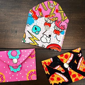 May include: Three fabric envelopes with different patterns. The first envelope has a pink and white pattern with a cherry and ice cream design. The second envelope has a pink and white polka dot pattern with a donut design. The third envelope has a black and white pattern with a pizza design.
