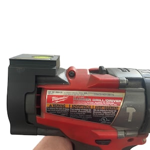 May include: A red and black Milwaukee 18V Hammer Drill/Driver with a level on top. The drill has a 1/2 inch chuck and a maximum speed of 3500 RPM. The drill is made in China and has a UL listing.