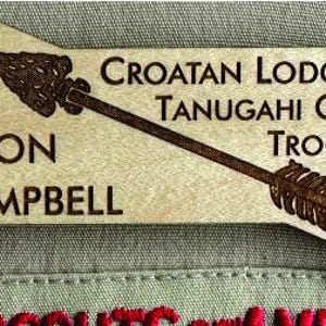 May include: A wooden name tag with a brown arrow design. The text on the tag reads "Croatan Lodge 117 Tanugahi Chapter Troop 743" and "Jason Campbell".