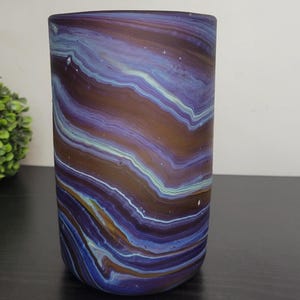 May include: A cylindrical vase with a swirling pattern of blue, brown, and white. The vase is made of glass and has a smooth, polished surface. The vase is approximately 6 inches tall.