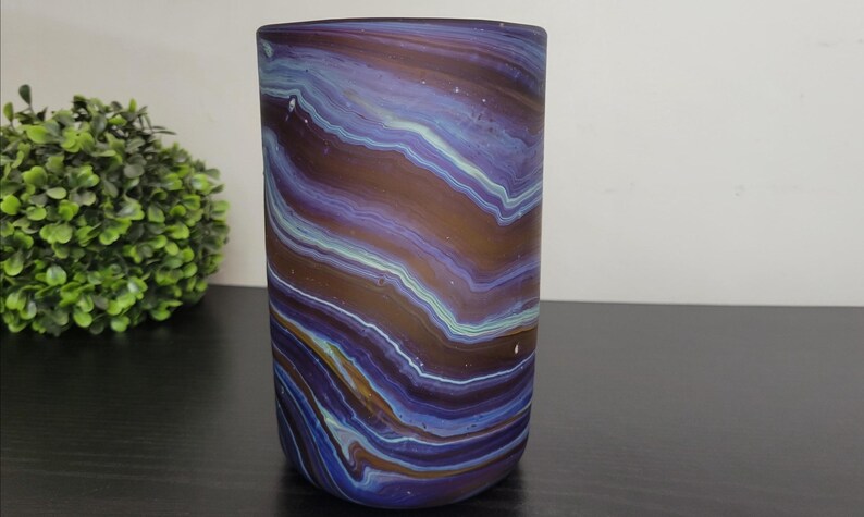 May include: A cylindrical vase with a swirling pattern of blue, brown, and white. The vase is made of glass and has a smooth, polished surface. The vase is approximately 6 inches tall.