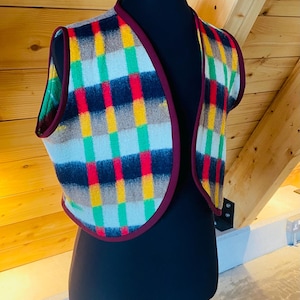 May include: A sleeveless vest with a plaid pattern in shades of red, yellow, green, blue, and brown. The vest has a burgundy trim.