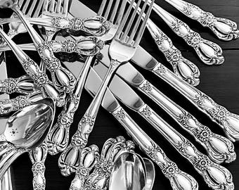 May include: A collection of silver-toned flatware including forks, knives, and spoons. Each piece features an ornate, embossed floral pattern on the handle. The utensils are arranged in a scattered, overlapping pile, showcasing the metallic finish.