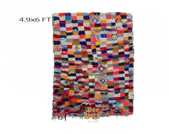 May include: A colorful Moroccan rug with a geometric pattern in shades of red, blue, orange, and white. The rug is 4.9 x 6 feet.