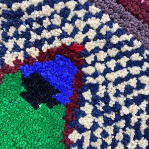 May include: Close-up of a colorful rug with a geometric pattern. The rug is made of wool and has a variety of colors, including blue, green, red, and white.