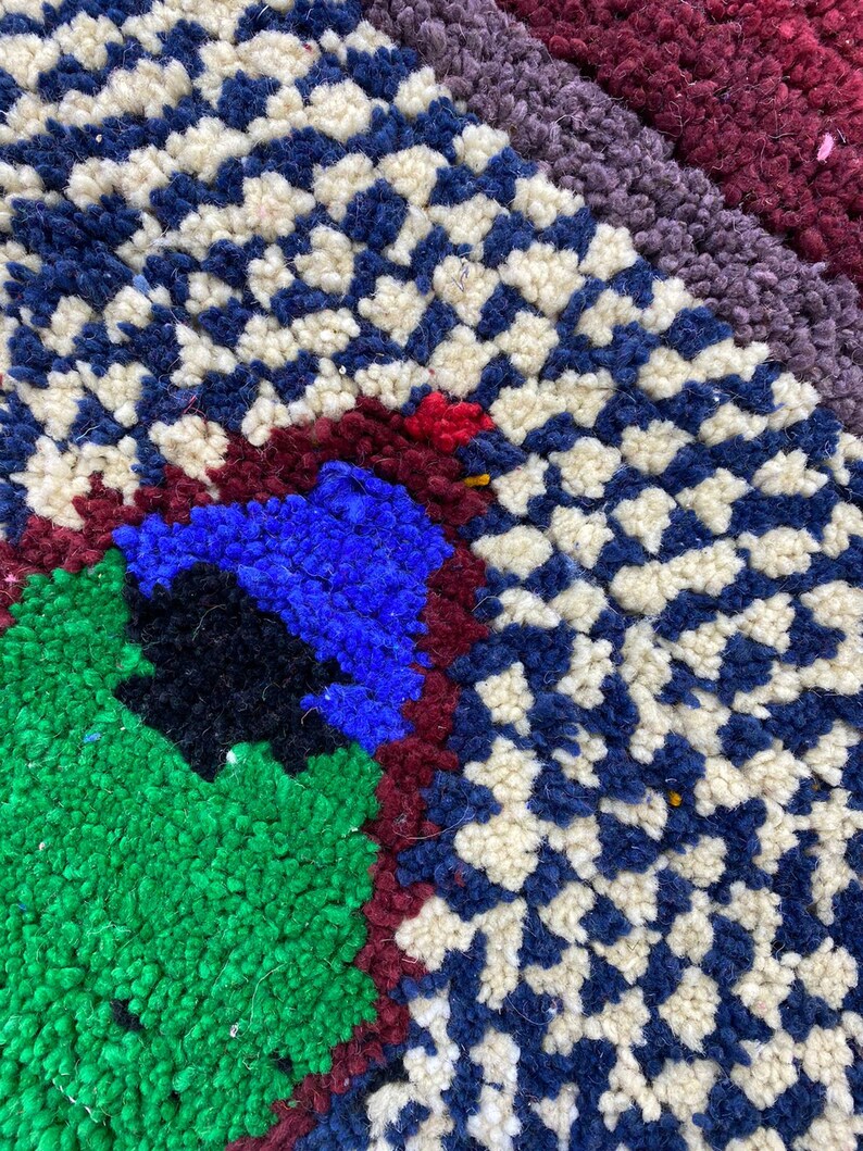 May include: Close-up of a colorful rug with a geometric pattern. The rug is made of wool and has a variety of colors, including blue, green, red, and white.