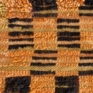 May include: Close-up of a woven rug with a geometric pattern in shades of orange, brown, and black.
