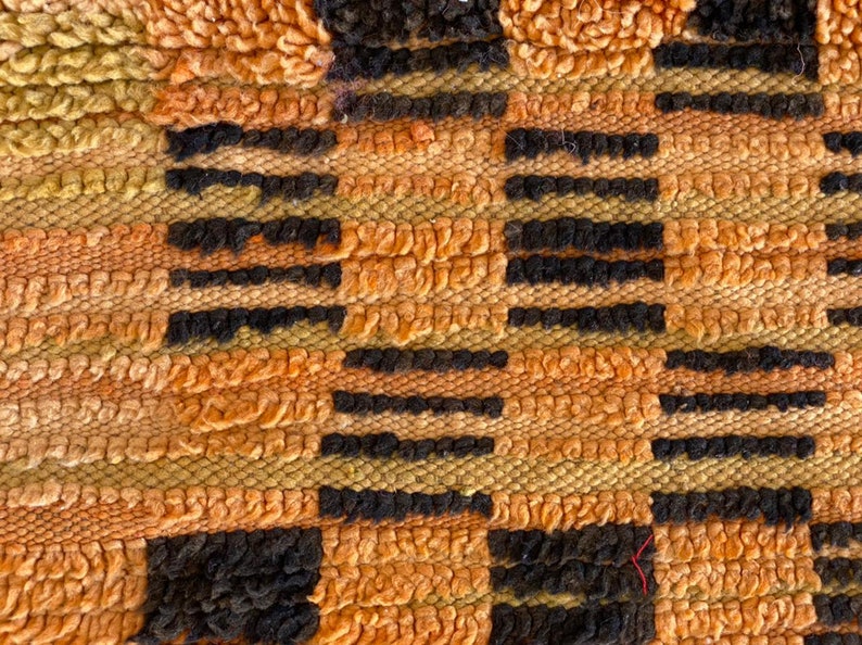 May include: Close-up of a woven rug with a geometric pattern in shades of orange, brown, and black.