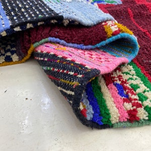 May include: A colorful woven rug with a variety of patterns and textures. The rug is made up of different sections of fabric, each with its own unique design. The rug is folded in half, revealing the different layers of fabric.