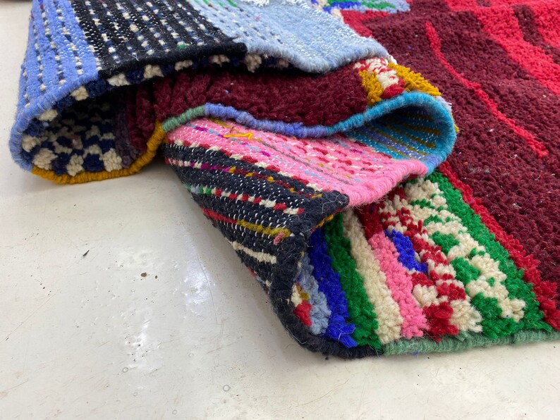 May include: A colorful woven rug with a variety of patterns and textures. The rug is made up of different sections of fabric, each with its own unique design. The rug is folded in half, revealing the different layers of fabric.