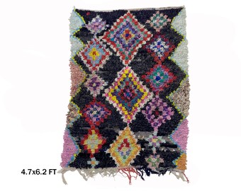 May include: A colorful Moroccan rug with a black background and a diamond pattern. The rug is approximately 4.7 feet by 6.2 feet.