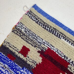 May include: A colorful striped rug with a geometric pattern in shades of red, blue, white, and gray. The rug is made of a soft, fluffy material and has a fringe border.