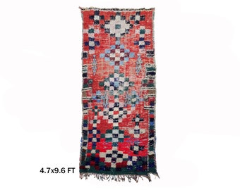May include: A red, blue, green, and white Moroccan rug with a geometric pattern. The rug is 4.7 feet wide and 9.6 feet long.